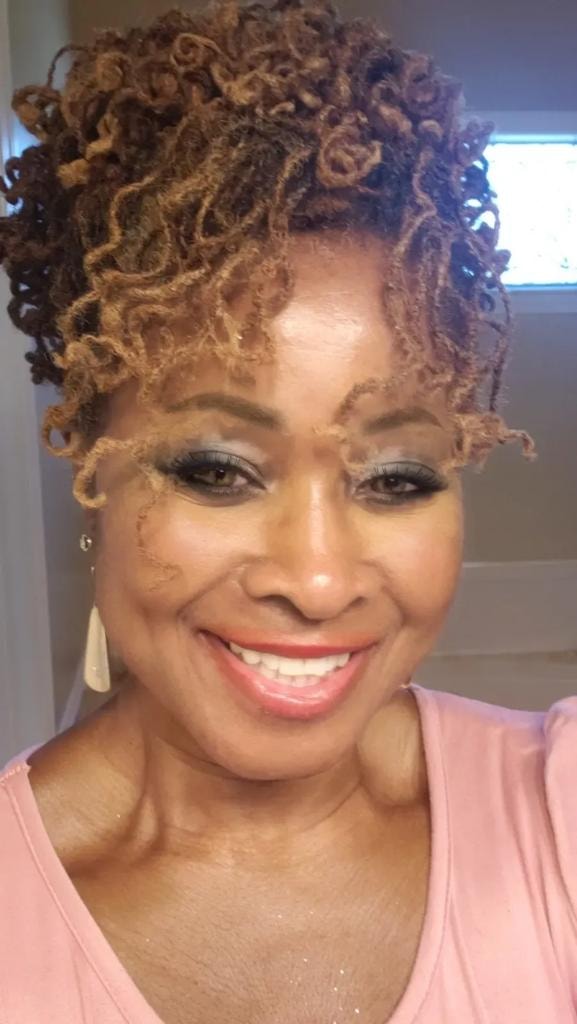 Short golden curly locs in pink top smiling