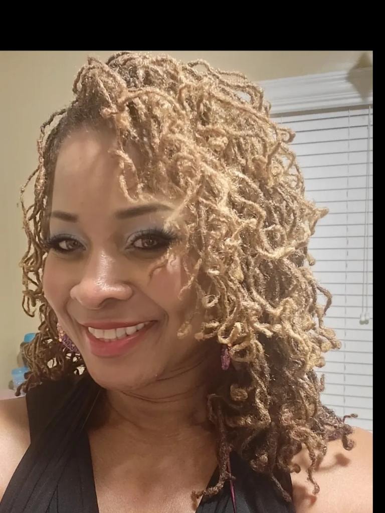 Woman with twisted locs smiling in front of green wall